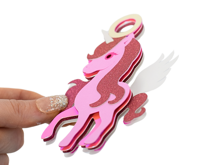 a hand holding a pink and white paper cut out of a horse
